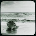 A rowing boat from the Eider on the shore with a rough sea behind. The plate has a J. Dore sticker on it and is captioned 'The Wreck of the Eider - the boat of the Eider. The Eider was carrying maize, cotton, gold, silver and mail when she ran aground on Atherfield Ledge on 31st January 1892. Salvage continued until 29th March when she was towed to Southampton