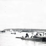 Harbour scene at an unidentified location although probably Cowes. A small steam launch is landing at a jetty in the foreground and a paddle steamer is in the background