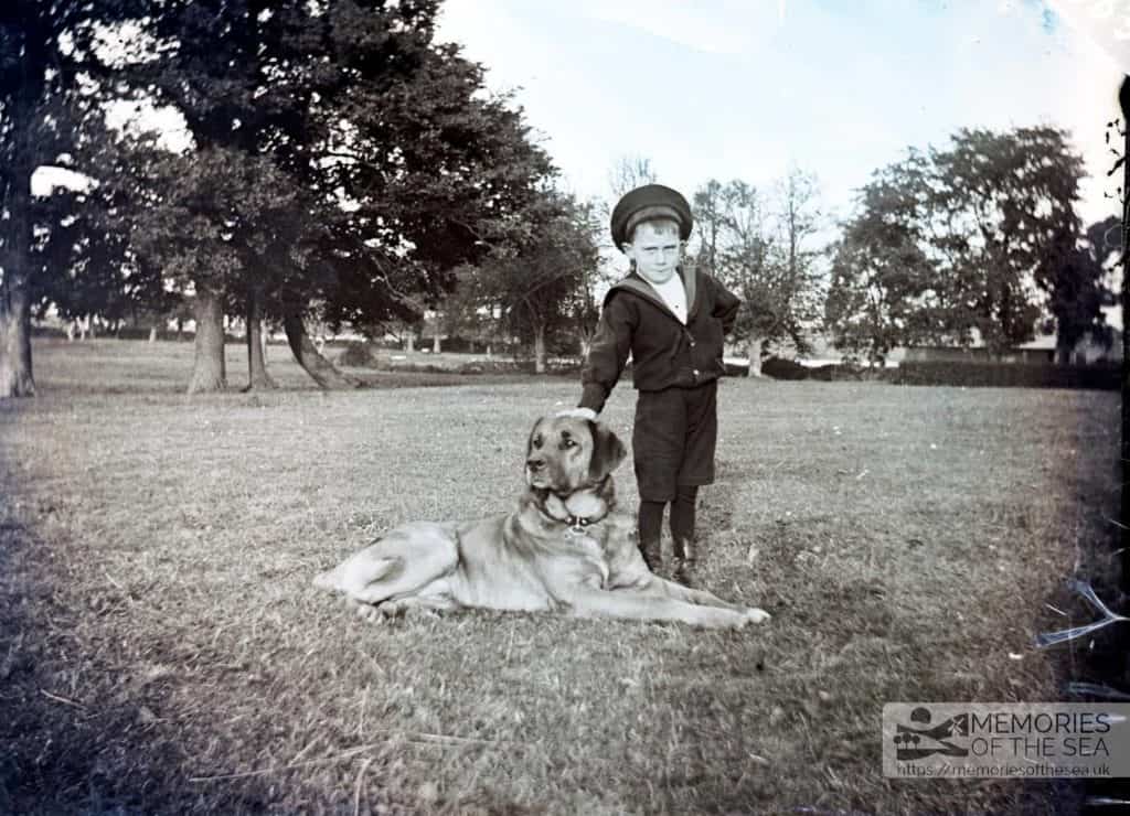 Boy in a sailor suit standing next to a Labrador