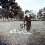 Boy in a sailor suit standing next to a Labrador