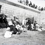 People seated on a beach against the sea wall. Probably Sandown or Shanklin