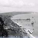 View of Sandown Bay from the cliffs, bathing huts visible on the beach and boats on the water