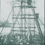 Crowds watching men at the top of a scaffolding tower in 1912. The plate is captioned, but the word before 'drill' is illegible. A pier can be seen in the background, presumably Sandown