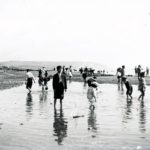 Children playing on Sandown Beach. Small boy with toy sailing boat in foreground