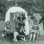 Four young women on the beach, a fisherman stands nearby