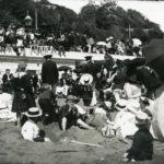 Crowd on a beach at Sandown entertained by musicians. The photographer is J. Dore and the image is entitled Watching the Niggers it dates between 1890 and 1914