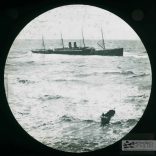 The wreck of the Eider as viewed from the beach, a small boat is rowing to shore. The plate has a J. Dore sticker on it and is captioned 'The Wreck of the Eider - the boat of the Eider. The Eider was carrying maize, cotton, gold, silver and mail when she ran aground on Atherfield Ledge on 31st January 1892. Salvage continued until 29th March when she was towed to Southampton