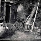 Two fishermen sitting outside a wooden hut making crab pots