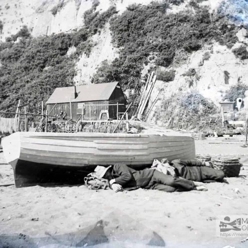 Two fisherman asleep underneath a boat on the beach