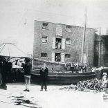 Workers pose outside a warehouse by Newport Quay. Some stevedores pose on a barge. Warehouse belongs to Croucher and sons and is now Rope store gallery at the Quay Arts centre